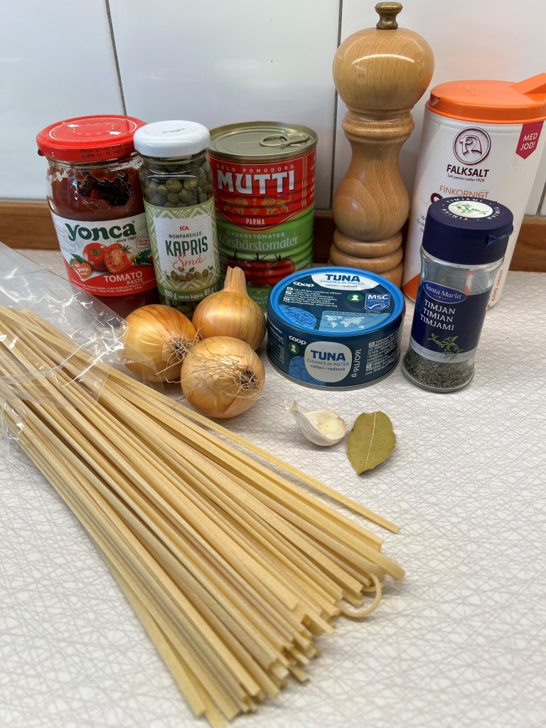 En uppsättning av ingredienser för att laga pasta, inklusive tomatpasta, kapris, körsbärstomater, tonfisk, lök, vitlök, lagerblad, samt kryddor som timjan och salt.