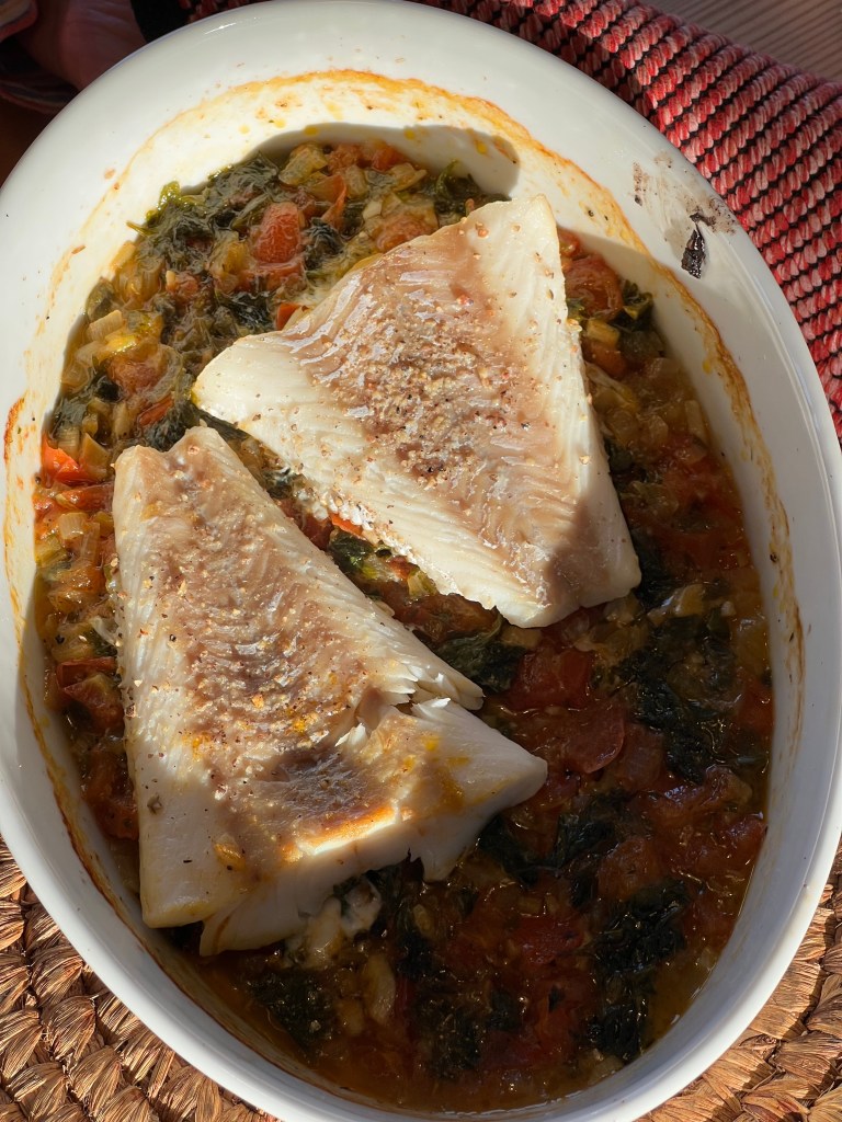 En ugnsbakad fiskfilé med grönsaker i en vit form, omgiven av en naturlig matta.