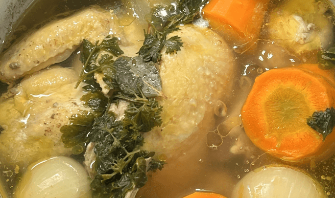 En gryta med kyckling, morötter, lök och färsk persilja i en klar buljong.