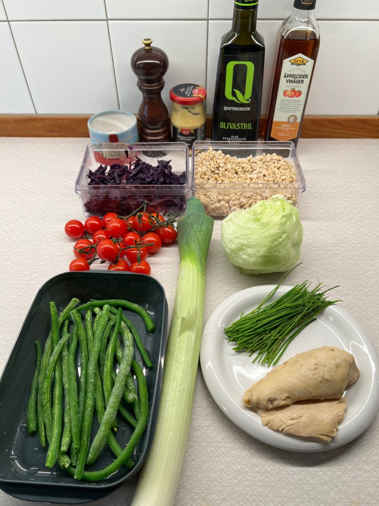 En samling färska ingredienser för matlagning, inklusive gröna bönor, körsbärstomater, purjolök, isbergssallad, ingefära, rödkål, pärlkorn samt olika kryddor och oljor.