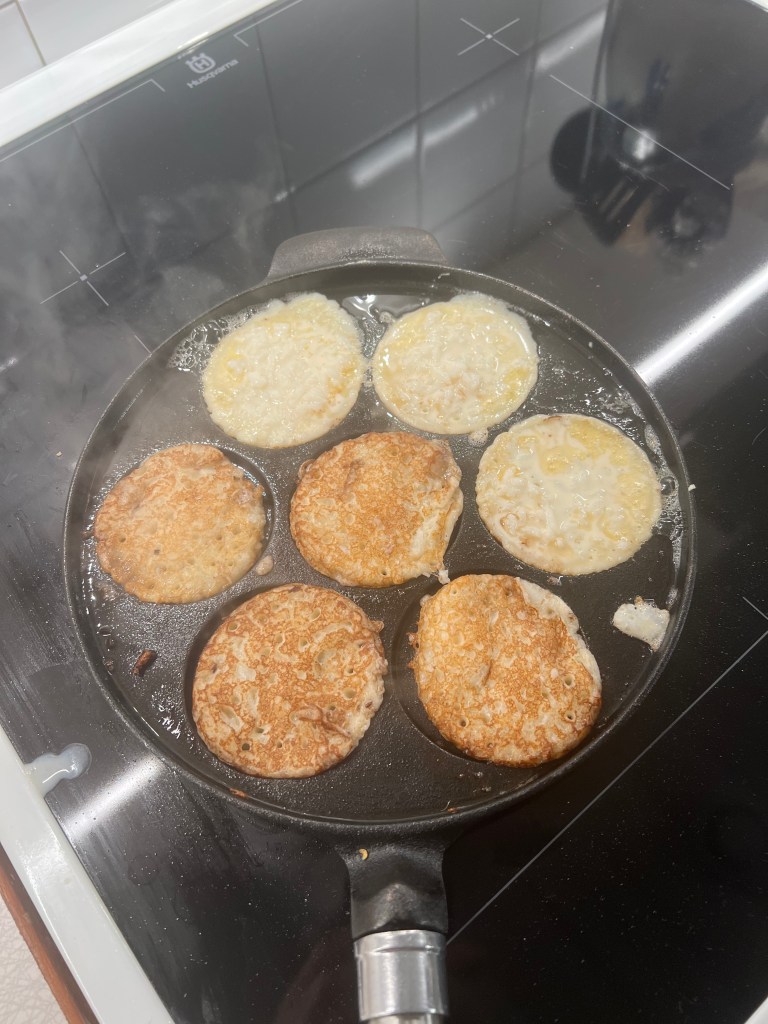 En stekpanna med sju platta pannkakor som fräser på en induktionsspis, med ånga som stiger upp.